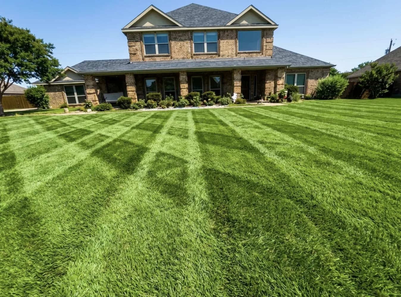 A Rockwall brick home with fresh mowing stripes and healthy trees and shrubs cared for by Green Lawn Fertilizing